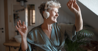Mulher sênior feliz com fones de ouvido dançando em casa, relaxando e conceito de autocuidado.