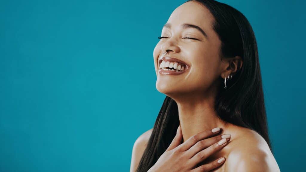 Imagem de fundo azul e em destaque uma mulher feliz e sorrindo, apresentando o conceito de como é bom se sentir bem consigo mesmo