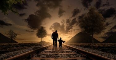 Imagem de uma estrada de ferro e em destaque pai e filho caminham sobre ela de mãos dadas.