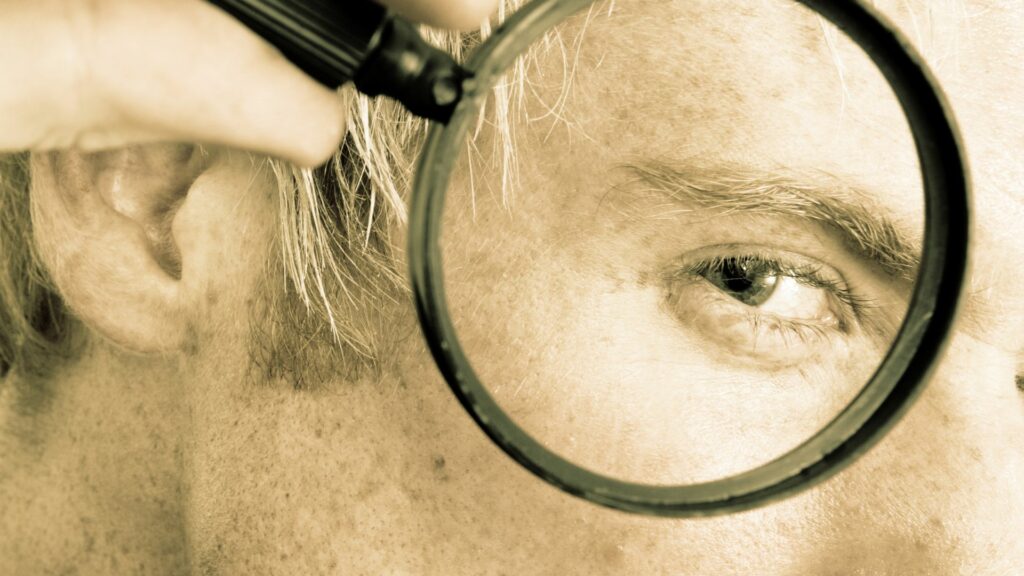 Imagem de um homem segurando uma lupa próximo ao seu olho, transmitindo o conceito de pura verdade, buscando a verdade.