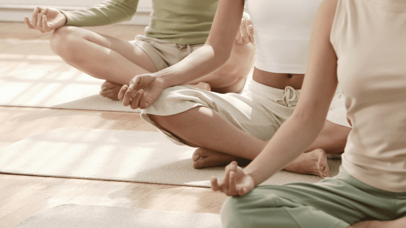 Mulheres sentadas em fileira, fazendo Yoga.