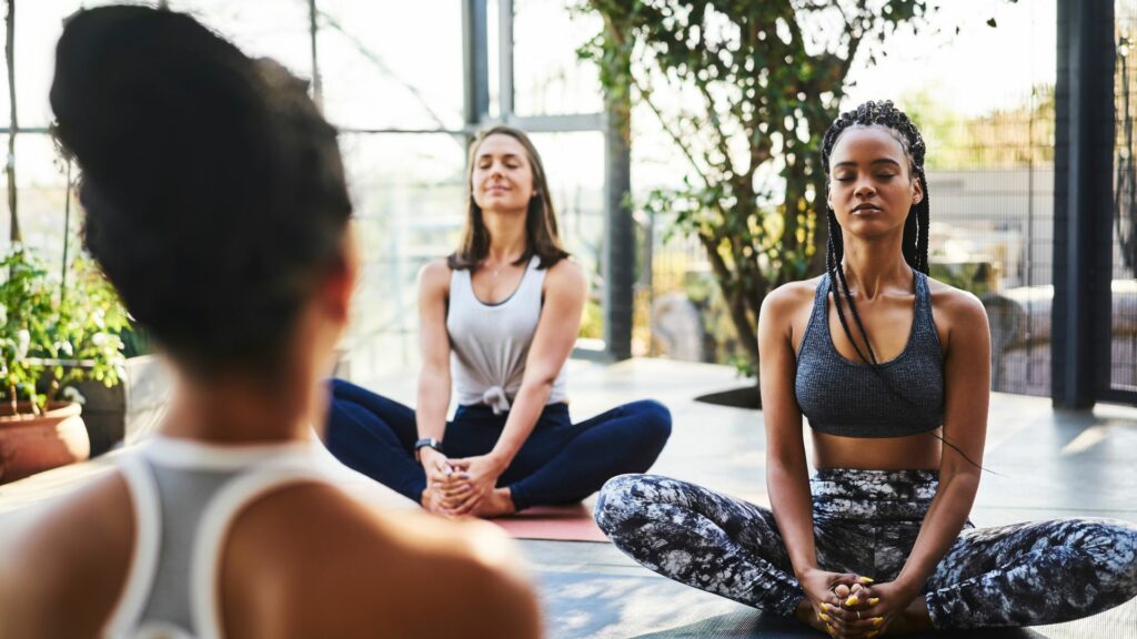 Mulheres meditando com instrutora durante aula de ioga.