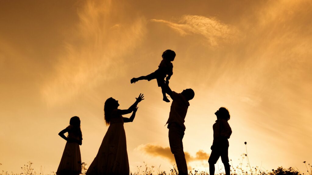 Imagem de fundo com um lindo pôr do Sol e em destaque a silhueta de uma família composta por pais e filhos.
