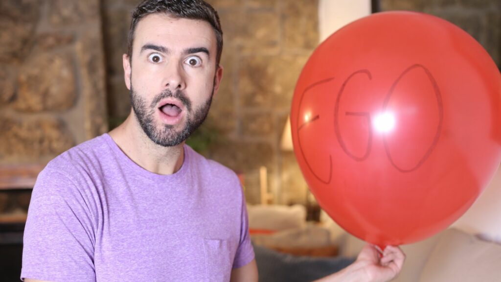 Homem segurando um grande balão vermelho representando seu ego.