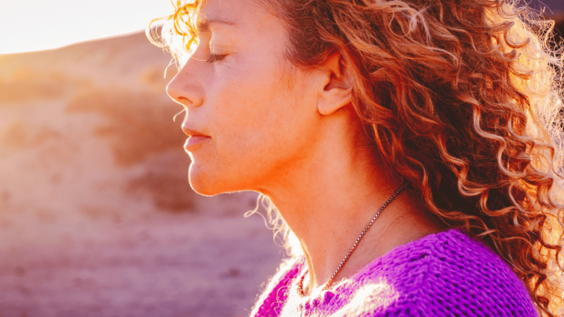 Retrato de uma mulher com os olhos fechados, sentindo o pôr do sol em sua face.