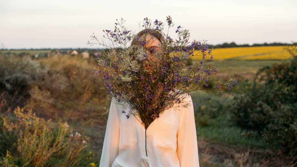 Imagem de um campo verde e em destaque uma mulher vestindo uma camisa branca celebrando a sua beleza interior e amor próprio. 
