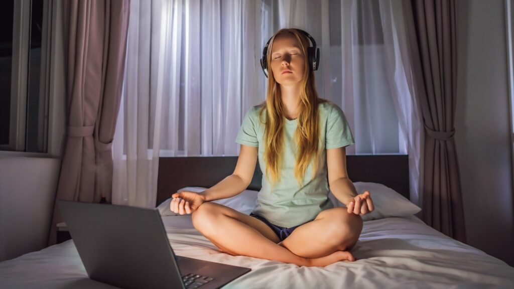 Mulher medita na cama usando aplicativo de meditação. Conceito de esporte, tecnologia e estilo de vida saudável.