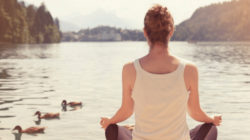 Mulher meditando em frente de lago.