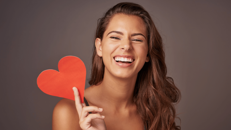 Mulher sorrindo enquanto segura coração vermelho de papel.