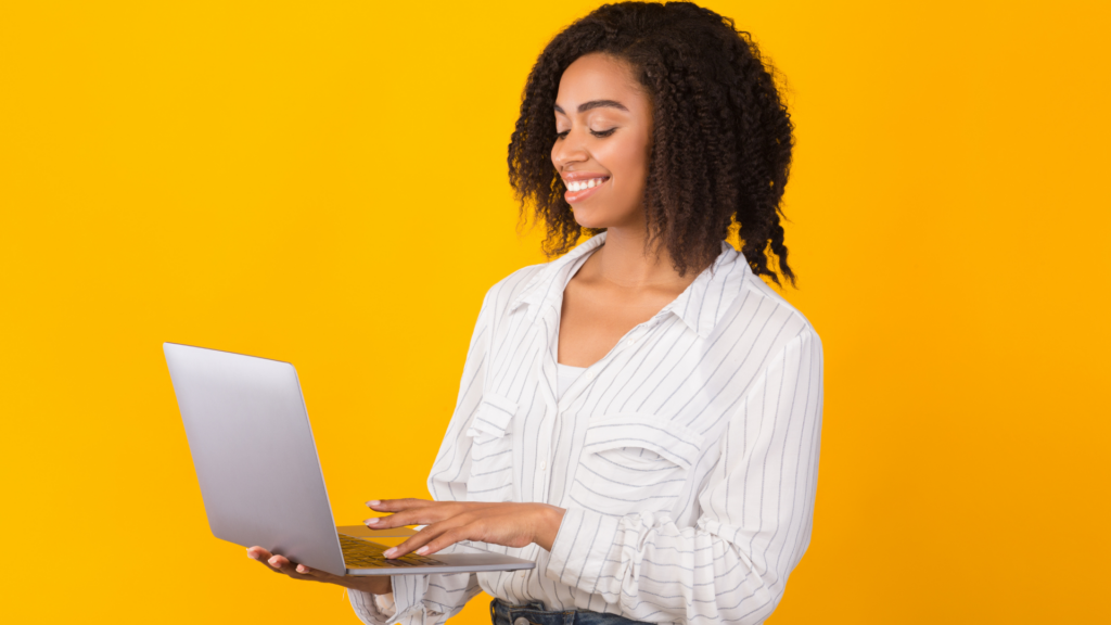 Mulher segurando computador em mãos, sobre fundo amarelo. 