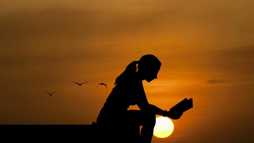 Imagem de fundo de um lindo pôr do sol e em destaque a silhueta de uma mulher lendo um livro, representando o conceito de busca pela paz.
