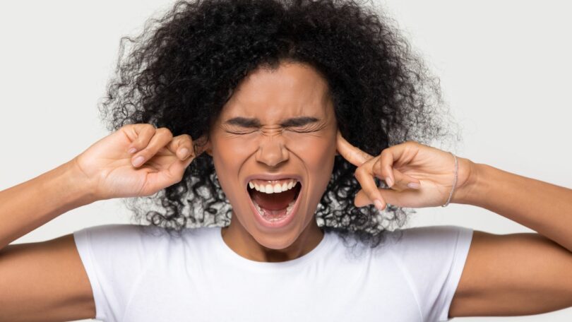 Imagem de uma mulher negra, gritando, teimosa e irritada enfiando os dedos nos ouvidos.