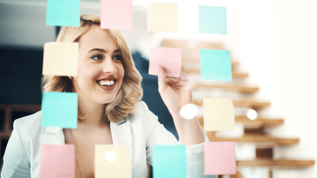 Mulher de negócios feliz, fazendo um brainstorming com nota adesivas na janela de vidro.