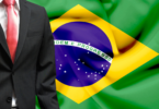 Homem vestido de terno. Ao funo, a bandeira do Brasil. Conceito de candidato político.