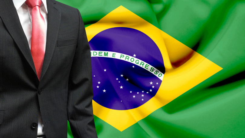 Homem vestido de terno. Ao funo, a bandeira do Brasil. Conceito de candidato político.