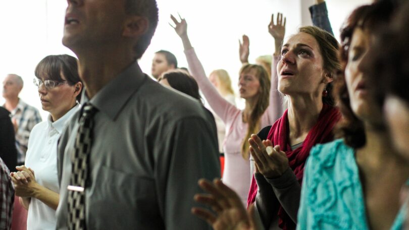 Imagen de várias pessoas, homens e mulheres, louvando a Deus dentro de uma igreja.