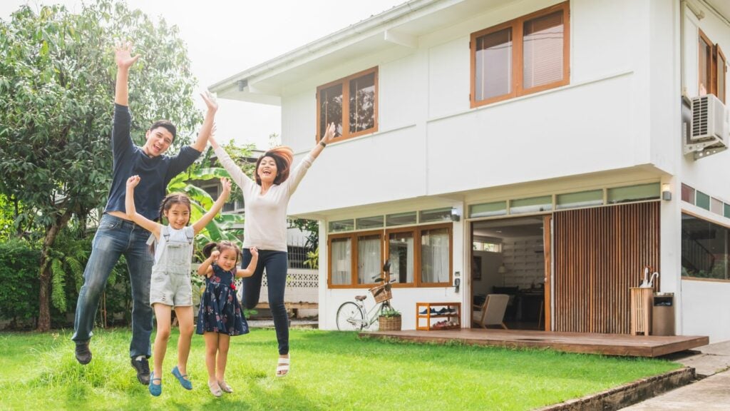 Imagem de uma família asiática na frente de casa, trazendo o conceito de casa, de ambiente doméstico e de família feliz.