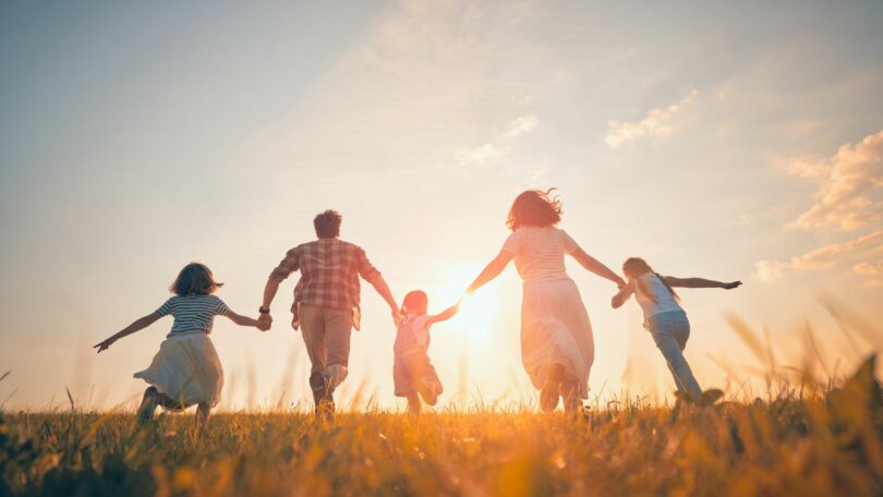 Imagem de uma família feliz, composta pelos pais e os três filhos, caminhando de mãos dadas sob o pôr do Sol.