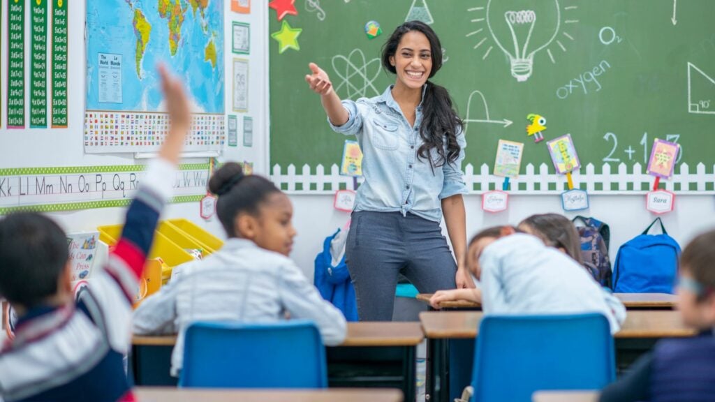 Imagem de uma professora em sala de aula junto com os seus alunos.
