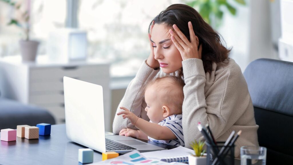 Imagem de uma mãe estressada com seu bebê trabalhando no escritório.
