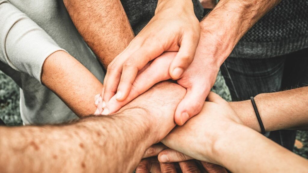 Imagem de várias mãos sobrepostas uma as outras, trazendo o conceito de liberdade, igualdade e fraternidade.
