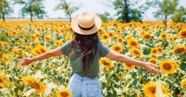 Imagem de uma jovem usando um chapéu de palha dentro de um campo de girassóis curtindo a natureza.