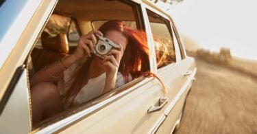 Imagem de uma moça dentro de um carro raridade, fazendo fotos dos momentos felizes e de lazer que está passando.