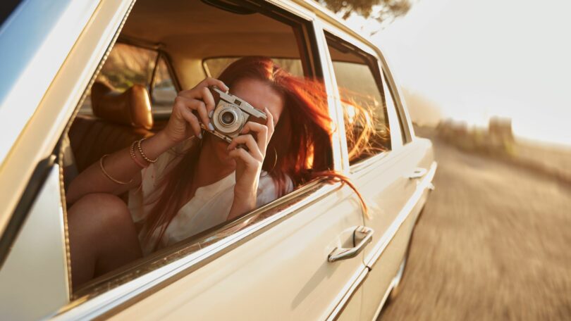 Imagem de uma moça dentro de um carro raridade, fazendo fotos dos momentos felizes e de lazer que está passando.