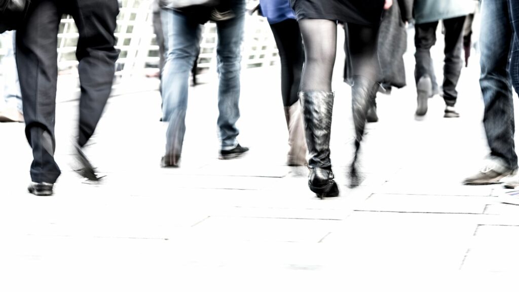 Imagem de várias pessoas caminhando em uma rua em uma cidade grande. A foto traz o conceito de agito, correria do dia a dia.
