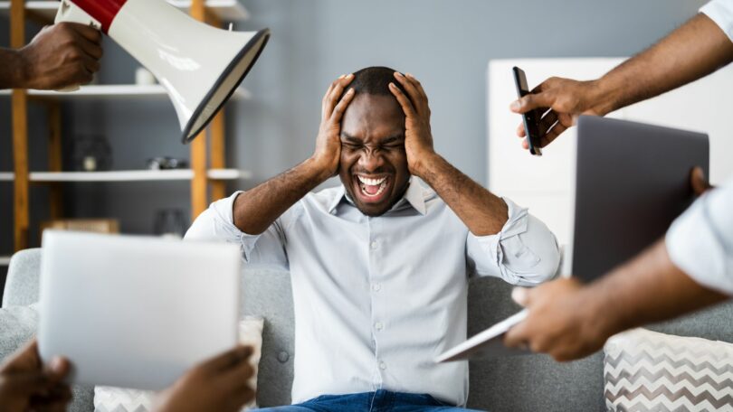 Imagem de um homem sentado em um sofá com as mãos na cabeça sendo bombardeado com notícias falsas e sobrecarga de conteúdo presentes nas redes sociais.