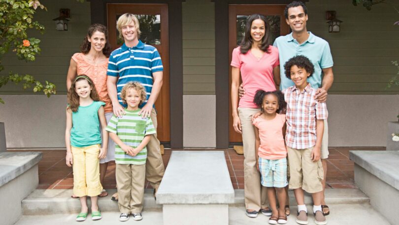 Imagem de duas famílias compostas por pais e filhos e são vizinhas. Elas estão na varada de suas casas, simbolizando o conceito de amizade e coletividade.