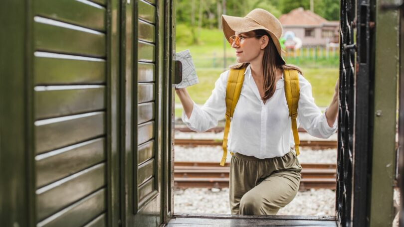 Imagem de uma linda mulher usando um chapéu de palha, mochila amarela nas costas, embarcando em um trem com destino à Paris, em uma viagem de férias e busca pelo seu eu e redenção.