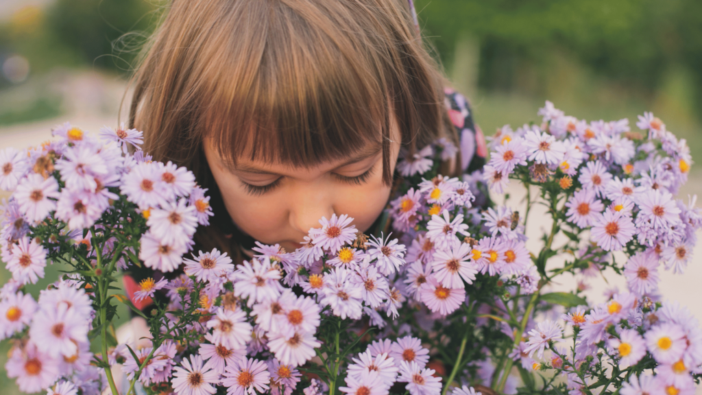 Uma menina e criança se curva e cheira flores da cor lilás.