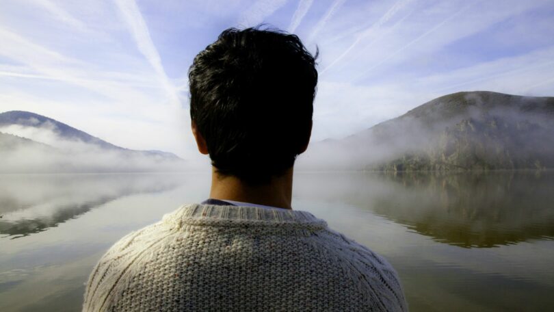 Imagem de um lago e em volta dele, duas montanhas. Em destaque, um homem, olhando para o futuro, trazendo o conceito de valorização da vida.