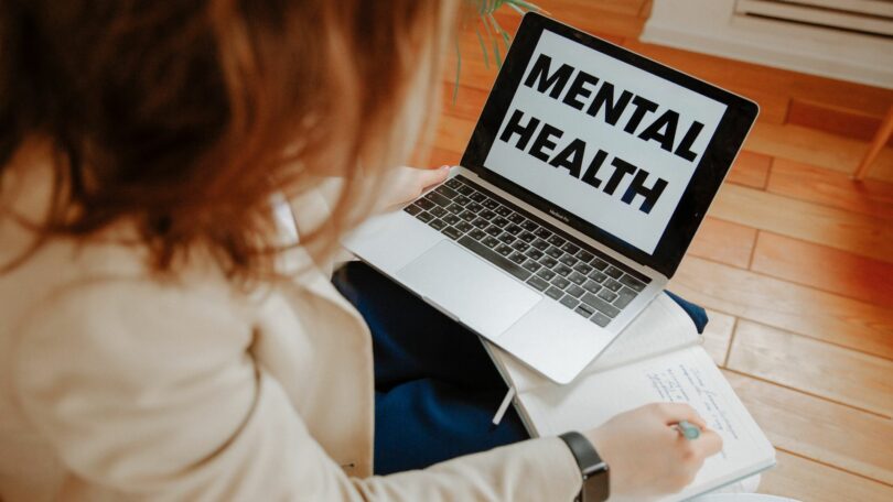 Imagem de uma mulher terapeuta tomando notas e usando o seu notebook sobre o seu colo.