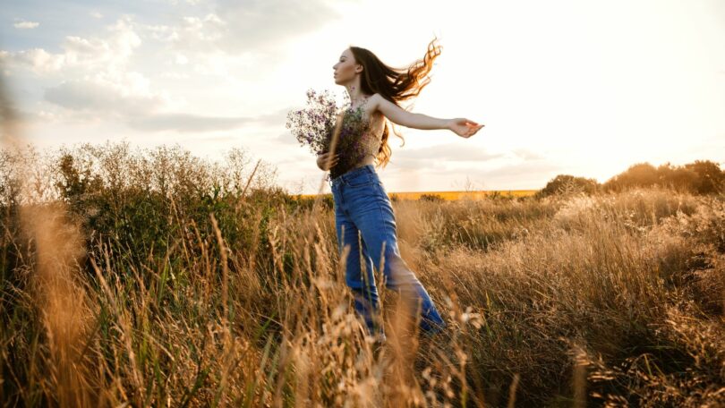 Imagem de uma mulher no campo segurando um ramalhete de flores, trazendo o conceito de renovação da alma.