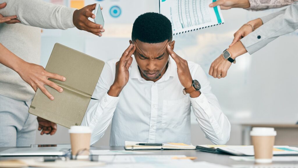 Imagem de um homem negro em seu local de trabalho. Ele está cansado, com excesso de trabalho, com problema de saúde mental e alto nível de ansiedade.