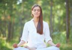 Imagem de uma mulher usando roupa branca. Ela está sentando em posição de yoga praticando a meditação e fazendo o hoponopono.