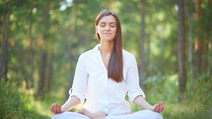 Imagem de uma mulher usando roupa branca. Ela está sentando em posição de yoga praticando a meditação e fazendo o hoponopono.