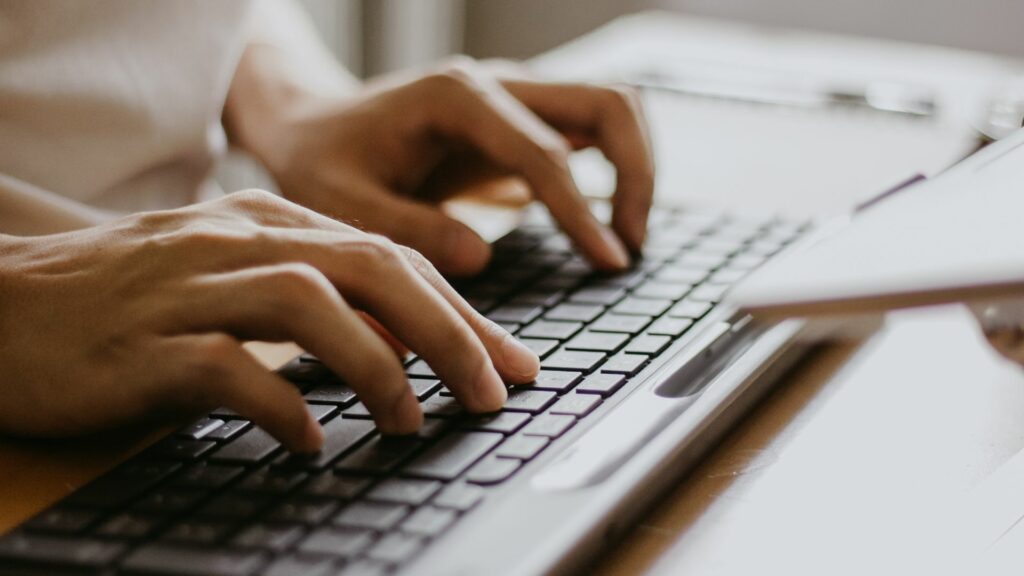 Imagem de mãos masculinas digitando em um teclado de computador sem fio, trazendo o conceito da relação entre o homem e a máquina.
