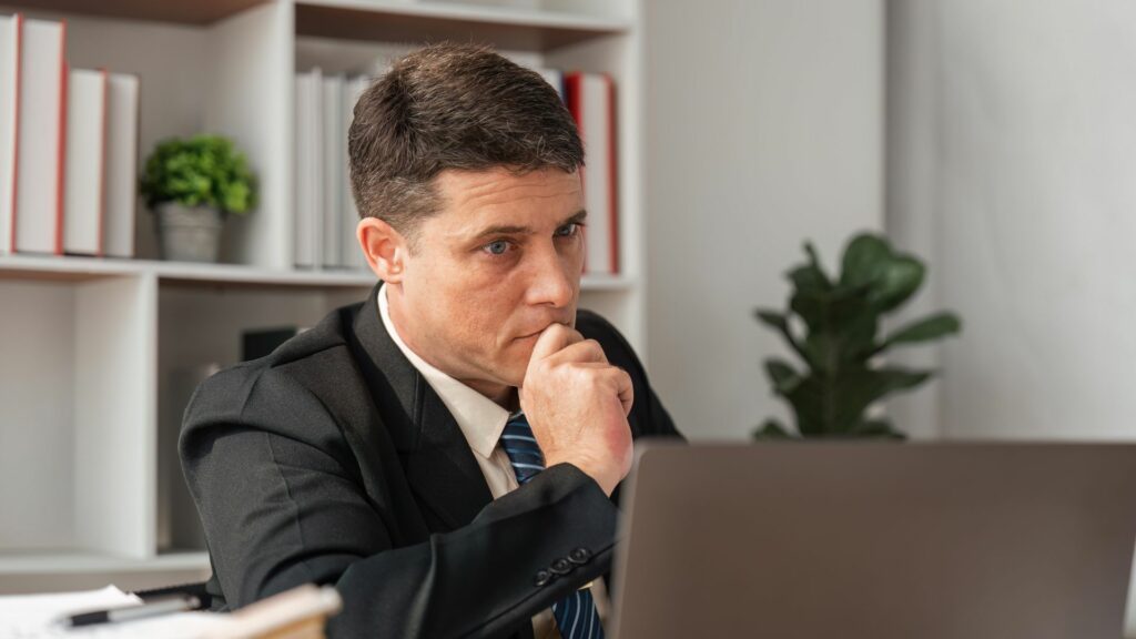 Imagem de um homem com semblante pensativo e questionador,  olhando para laptop, trazendo o conceito da relação entre homem e máquina e suas indagações.