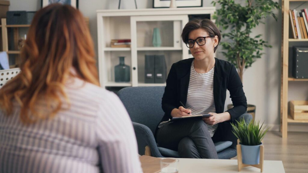 Imagem de uma mulher obesa, sentada de costas, conversando com uma psicóloga, procurando ajuda e apoio para lidar com a obesidade e a saúde mental.
