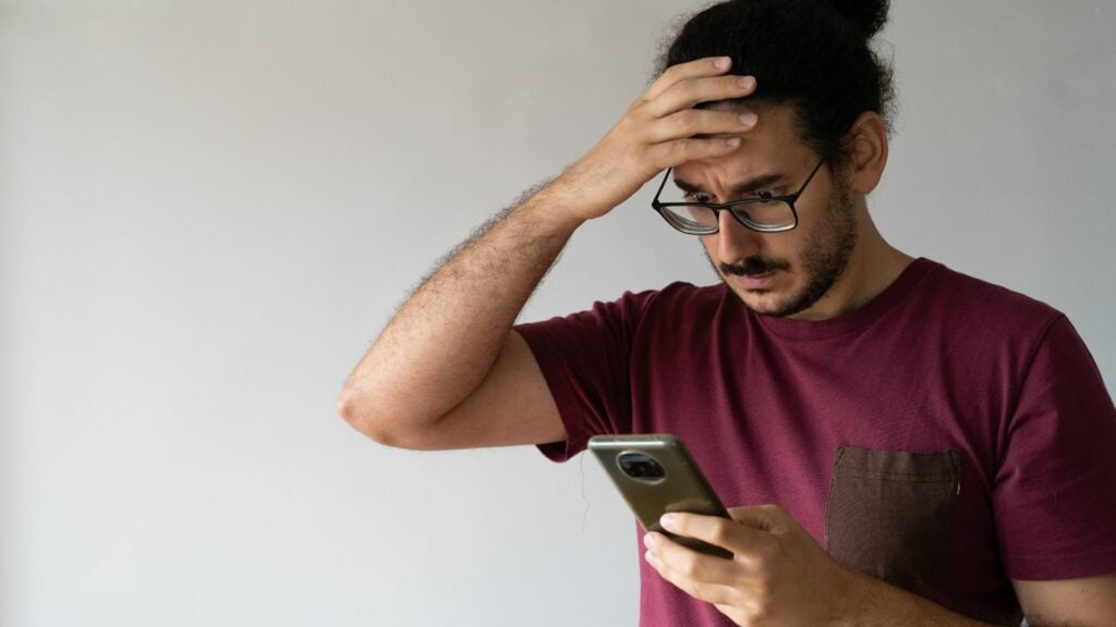 Imagem de um homem jovem ansioso lendo uma mensagem de texto em seu celular.
