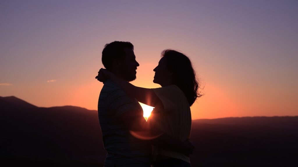 Imagem de um casal se abraçando ao ar livre ao pôr do sol.
